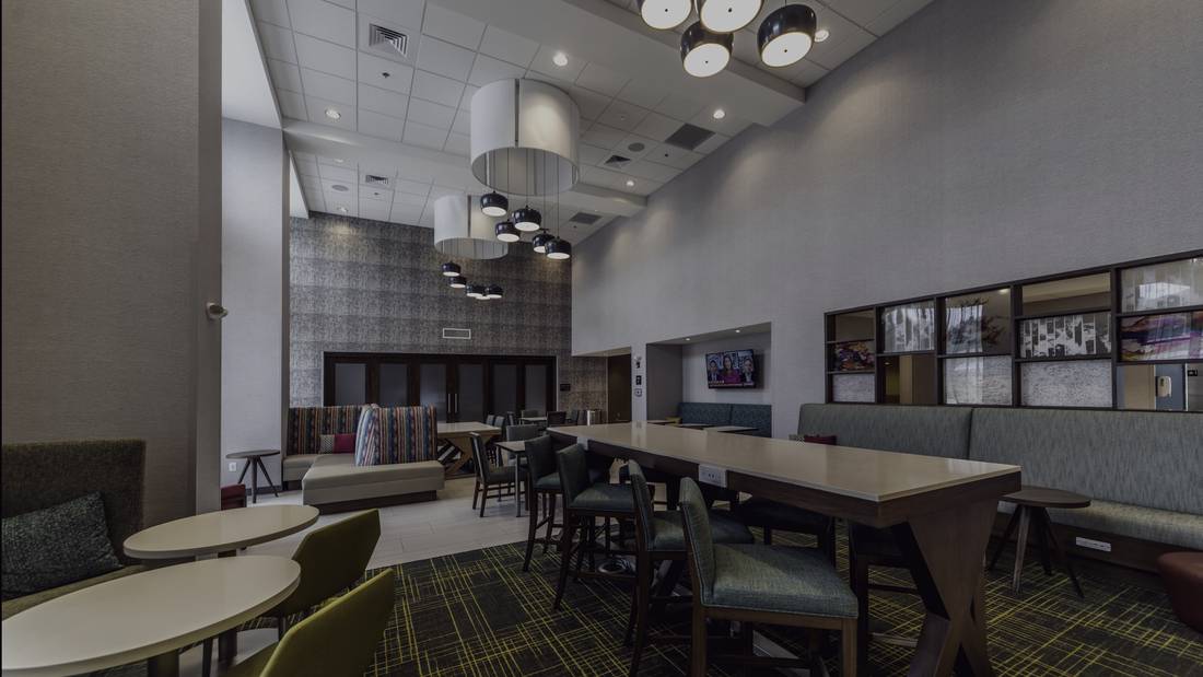 The great room at the Hampton Inn & Suites in Conway, Arkansas: communal table, upholstered chairs, pendant lighting and patterned broadloom.