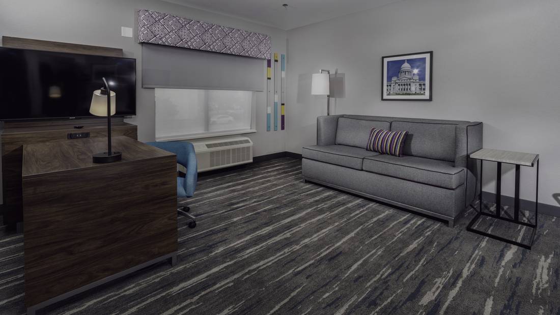Finished guestroom living area at the Hampton Inn & Suites, Conway: sleeper sofa, walnut casegood, table lamp, framed art, side table and broadloom carpet.