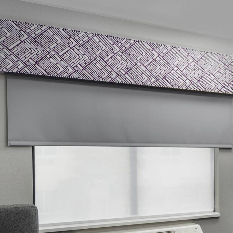 Patterned fabric valance over a roller shade and sheer in a guestroom window.