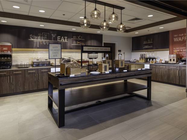Breakfast bar at Conway: walnut millwork, a communal serving table and smoked-glass globe pendants.
