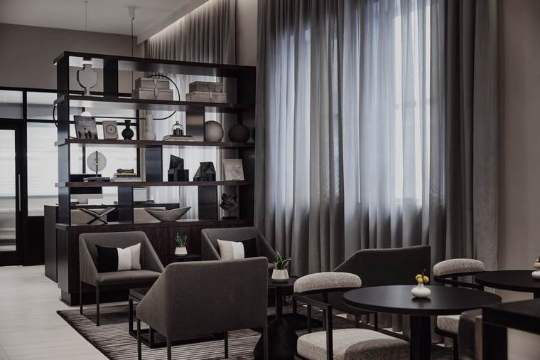 Library lounge at the AC Hotel Kansas City Downtown: blackened-steel open shelving, grey lounge chairs, bouclé stools, black round tables and floor-to-ceiling sheer drapery.
