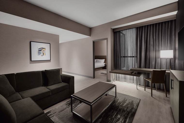King suite living area at the AC Hotel Kansas City Downtown: a sectional sofa, coffee table, desk and chair, floor lamp, area rug, framed art and layered drapery.