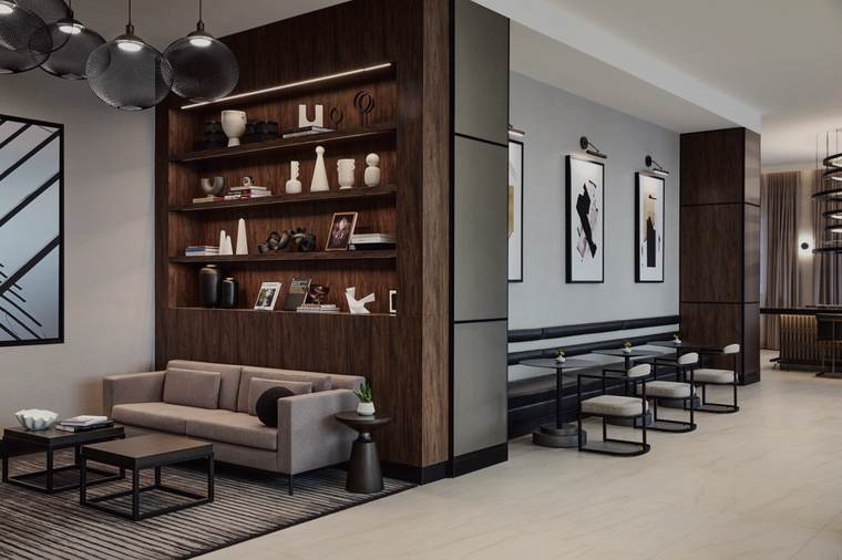 Lobby at the AC Hotel Kansas City Downtown: walnut display millwork styled with accessories, a tan sofa on a patterned rug, framed art, upholstered stools at a communal rail and a cluster of smoked-glass globe pendants.